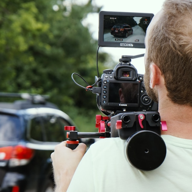 A high-end video production scene set in the picturesque region of Provence, South of France. The main subject is a professional video crew with high-end cameras and equipment setting up a shot in a lavender field. The composition should include the warm, golden hues of the setting sun casting a soft glow over the landscape, creating a romantic and tranquil atmosphere. The color palette should be vibrant, featuring the purple of the lavender fields, the green of the countryside, and the golden tones of the sunset. The camera angle should be from a low perspective, capturing both the intricate details of the lavender flowers and the expanse of the fields. The texture of the lavender flowers and the rugged ground should be evident. Environmental elements include distant rustic buildings and rolling hills. Props such as professional video cameras, tripods, and lighting equipment should be evident. The style should be photorealistic and ultra-detailed, similar to the works of photographers like Steve McCurry. Technical specifications: 8K resolution, hyperrealistic, with ultra-fine detail rendering.