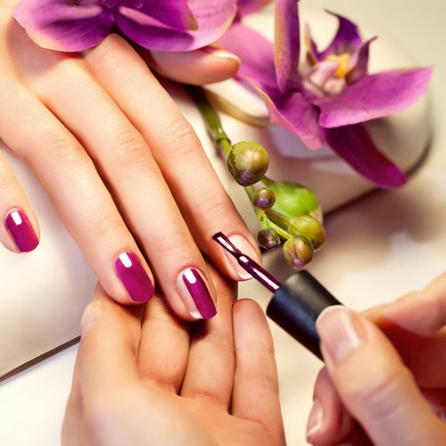 A photorealistic image of a spa pedicure setup, featuring a client with their feet in a bubbling foot bath, surrounded by candles and fresh flowers. Nail technicians are delicately applying shellac polish while a calming ambiance is depicted with soft lighting.