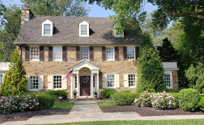Create a photorealistic image for the 'About Us' section of White Glove Pest Control. The scene should depict a close-up of a technician's hand, clad in a white glove, carefully releasing a captured spider outside of a home. The background is a blurred, lush green lawn and garden, bathed in soft, natural light. The spider should appear unharmed and the gesture should convey compassion and respect for nature. The composition should be balanced, with the hand as the focal point. Color palette: predominantly greens, browns, and whites, with highlights of natural light. Style: Emphasize cleanliness, care, and environmental responsibility. Technical specs: 4K resolution, high quality, depth of field to blur the background.
