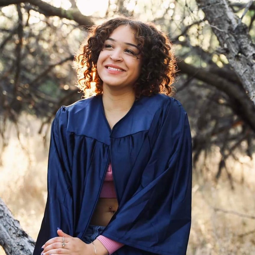 A joyful graduate in cap and gown, holding their diploma high in the air. The background features a university campus, with friends and family celebrating. Bright blue skies and colorful confetti floating in the air create a festive atmosphere.