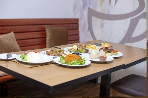 A 4K resolution, high-quality image depicting the essence of AH CAFE's mission. The scene should feature a diverse group of people laughing and enjoying a meal together at a large, communal table. The table is laden with a variety of colorful dishes representing local, continental, and vegan cuisines. The lighting is natural and warm, creating a sense of community and connection. The background is blurred to focus on the people and the food. The color palette should be bright and cheerful, with pops of color from the food, clothing, and decor. Capture the textures of the food, the smiles on people's faces, and the warmth of the atmosphere. The camera angle should be a medium shot, capturing the entire table and the people around it. Props include diverse food platters, serving bowls, and cheerful table decorations. Style reference: a blend of lifestyle photography and food photography.