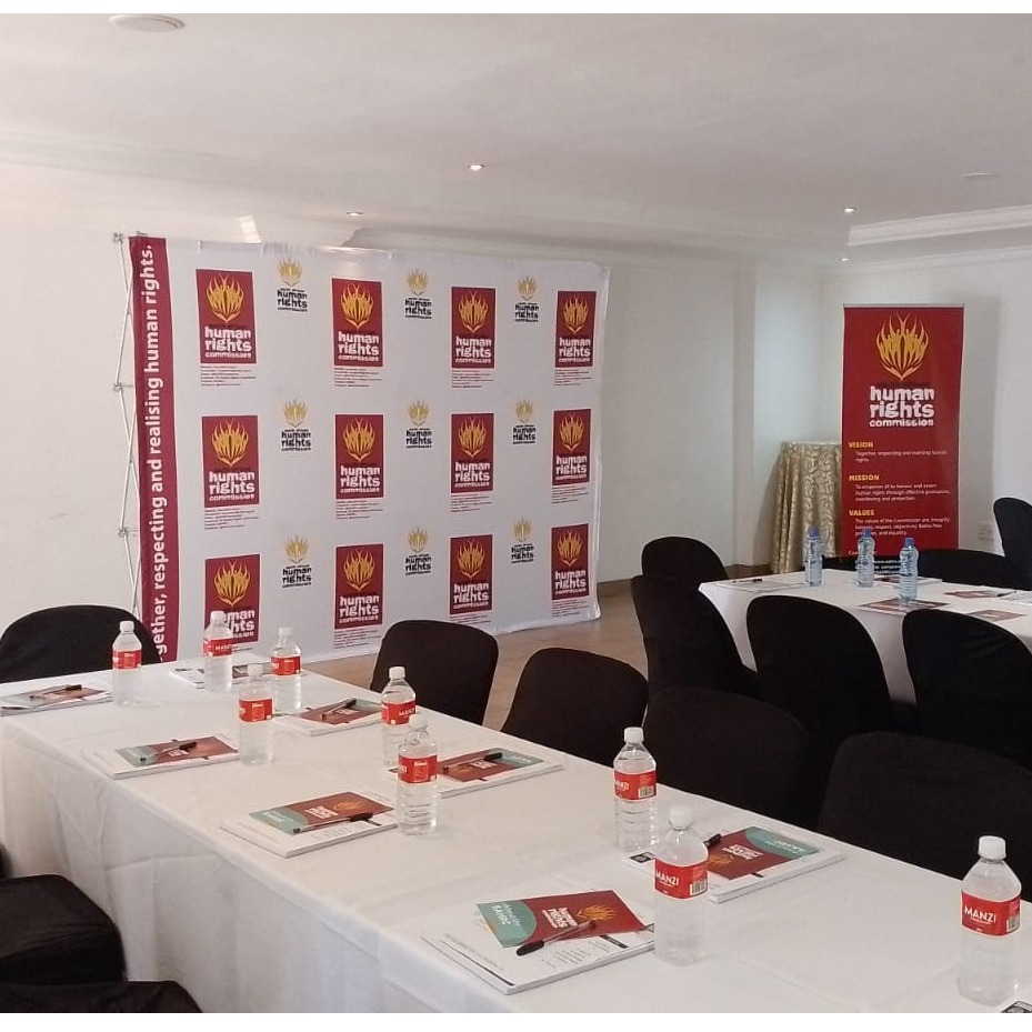 Create a 4k resolution, photorealistic image of a banquet hall set up for a corporate event at Magelevendze Lodge. The hall should be spacious and well-lit, with neatly arranged tables and chairs. Include a stage with a projector screen and a podium. The décor should be elegant and professional. Focus on creating a sense of order and functionality.