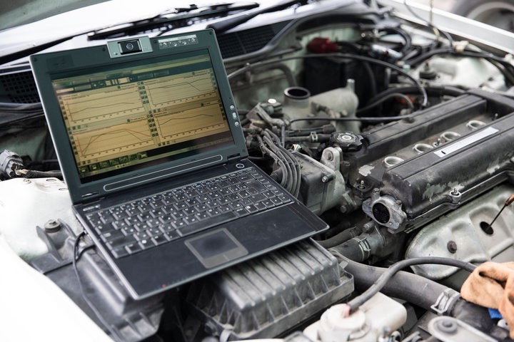 A close-up, photorealistic image of a mechanic using a diagnostic scan tool on a car's computer system. The focus should be on the tool's screen displaying complex data and the mechanic's focused expression. The background is slightly blurred, showcasing the interior of the car. The lighting is soft and diffused, highlighting the details of the equipment and the car's interior. Color palette should be professional with emphasis on the blue light from the diagnostic screen. Technical specs: 4K resolution.