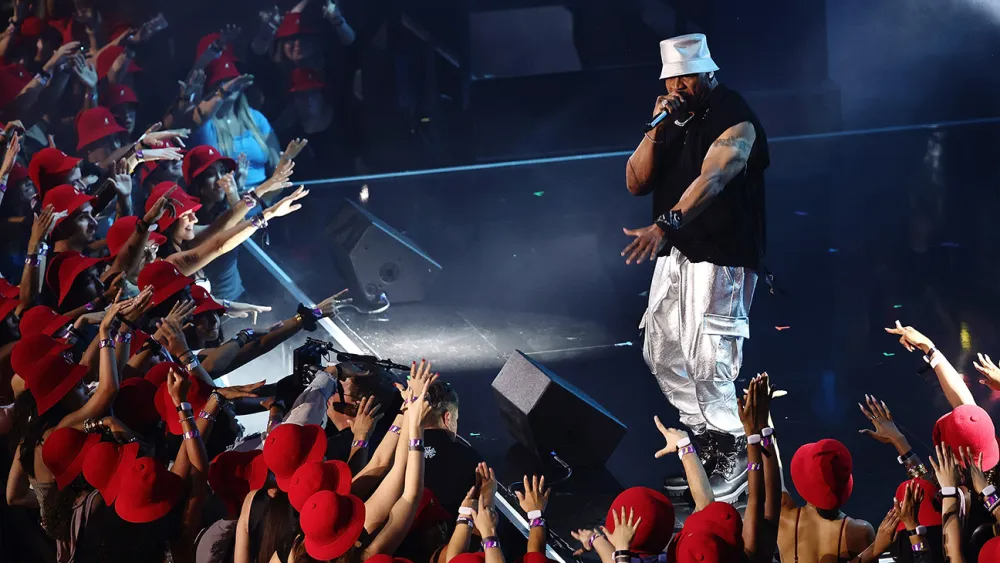 A stylized image of a hip-hop artist performing on a large stage, surrounded by enthusiastic fans. The lighting should be dramatic and atmospheric. The camera angle should focus on the artist. The style should be energetic and celebratory.