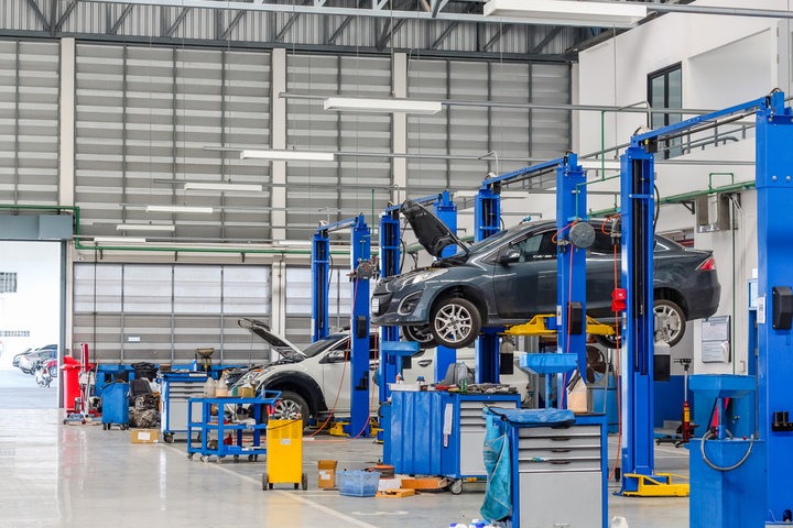 A photorealistic image of an auto repair shop showcasing diverse vehicles (cars, trucks, SUVs) undergoing different repair services. The image should convey a sense of bustling activity and competence. The lighting is bright and even, highlighting the various repair bays and mechanics working on different vehicles. Color palette is professional and clean. Technical specs: 4K resolution.