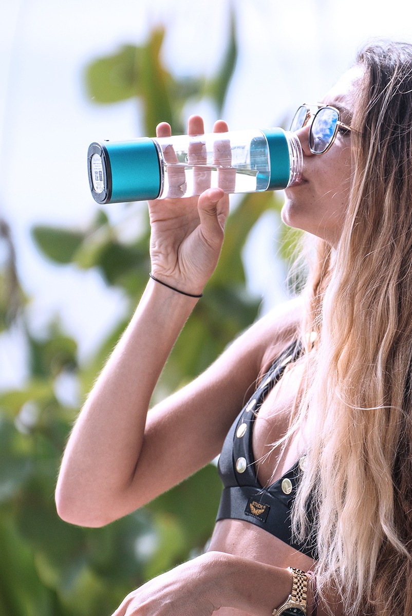 An athletic individual recovering after a workout, holding a bottle of hydrogen water. The background shows a gym setting with weights and exercise equipment, while an overlay graphic illustrates the concept of reduced inflammation and recovery.