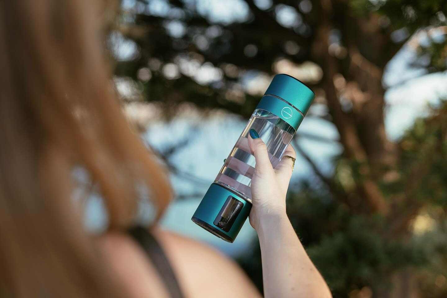 A fitness enthusiast in workout attire, holding a bottle of hydrogen water with a scenic park backdrop. The person appears energized and healthy, surrounded by fitness equipment like dumbbells and yoga mats, illustrating the health benefits of hydrogen water.