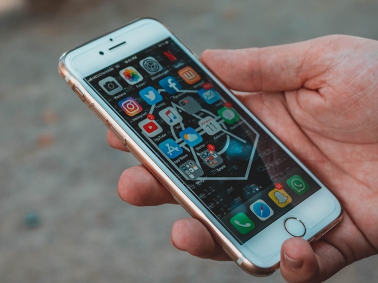 A hand holding a smartphone with a website displayed on the screen. The website shows a contact form with a large 'Send Us A Message' button. The background is a blurred image of a cityscape with a bright, sunny sky. The image should convey a sense of trust, openness, and accessibility.