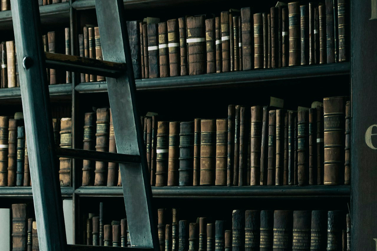 Create an image symbolizing brand authority and leadership. Depict a strong, confident tower of books, each representing a different aspect of industry knowledge and expertise. The books should be stacked neatly and securely, with a bright light shining down from above, illuminating them. Use a warm, inviting color palette to create a sense of trust and reliability. The background should be a blurred library or study setting. The overall style should be classic and sophisticated, emphasizing knowledge and experience. Camera angle: A low-angle shot looking up at the tower of books, emphasizing its height and strength. Texture details should highlight the aged paper and the leather bindings of the books.