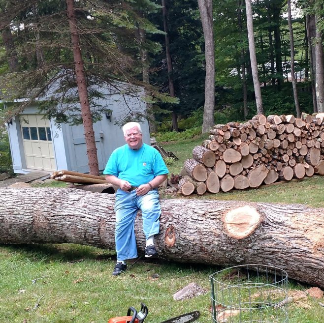 Tom Parker sitting on a fallen tree beside a woodpile