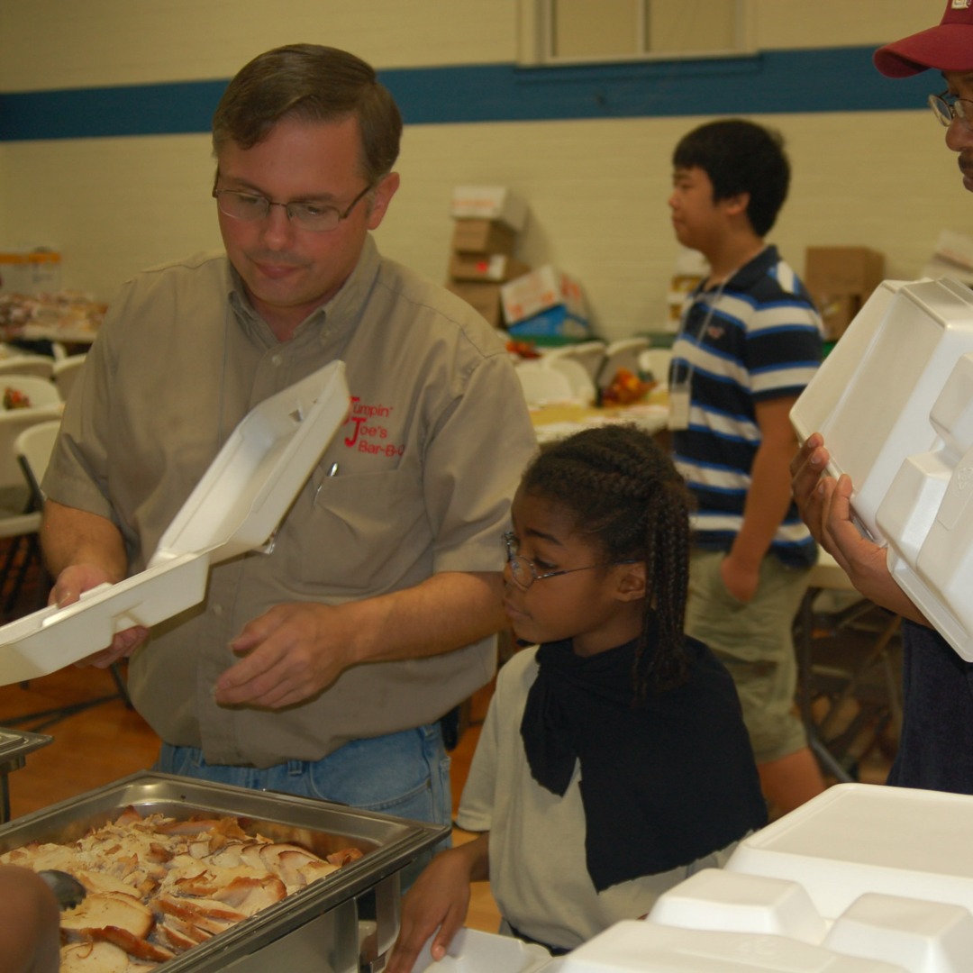 A person holding a takeout bag from a local restaurant, with a smartphone displaying a delivery app showing a donation option to a charity. In the background, a warm and inviting kitchen scene with fresh ingredients and busy chefs preparing food.