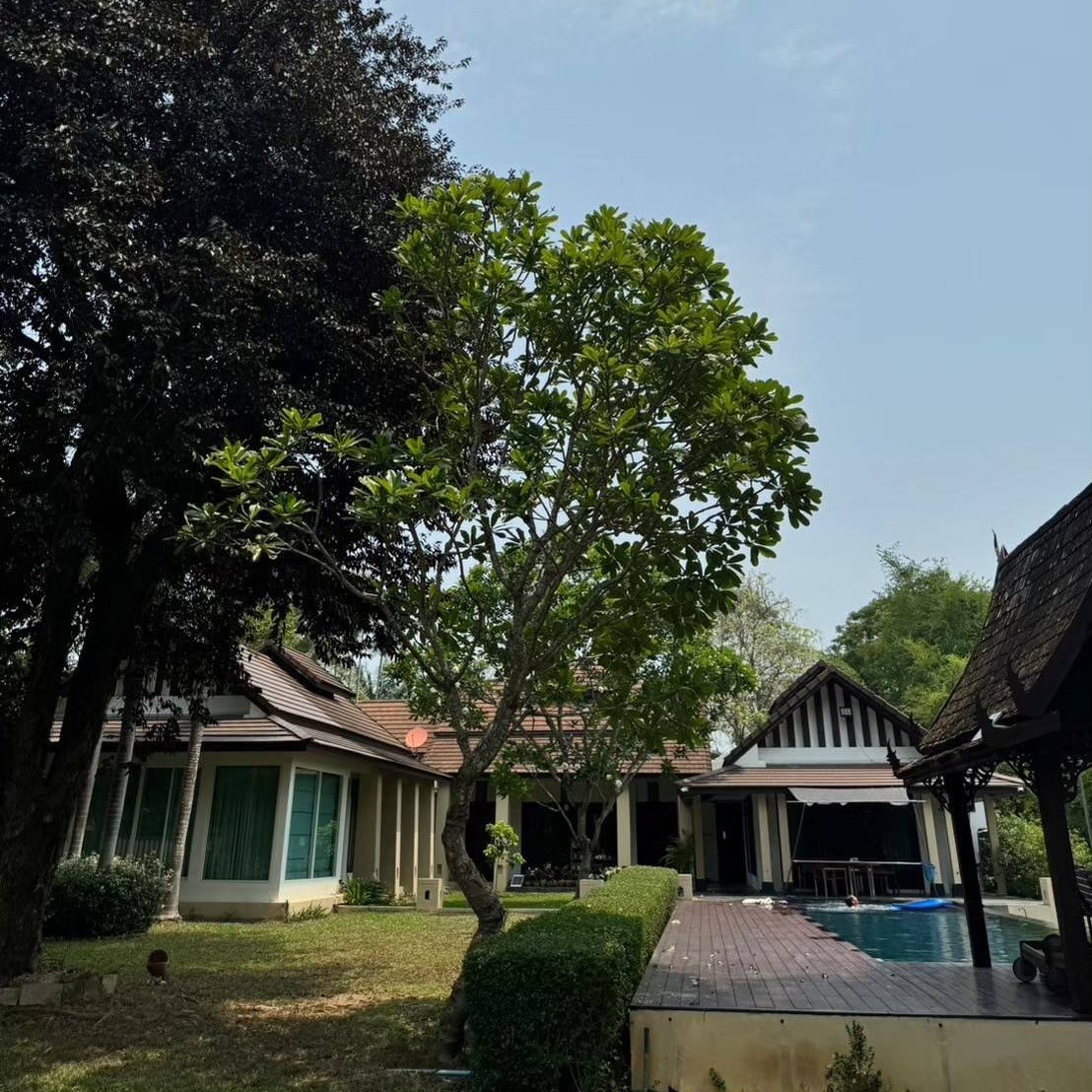 A photorealistic image showcasing the expansive grounds of a luxury property in Chiang Mai, Thailand.  The image should depict a large, well-maintained garden surrounding a modern house, with ample space for outdoor activities. The Ping River should be visible in the background.  The overall feeling should be one of spaciousness, serenity, and luxury.