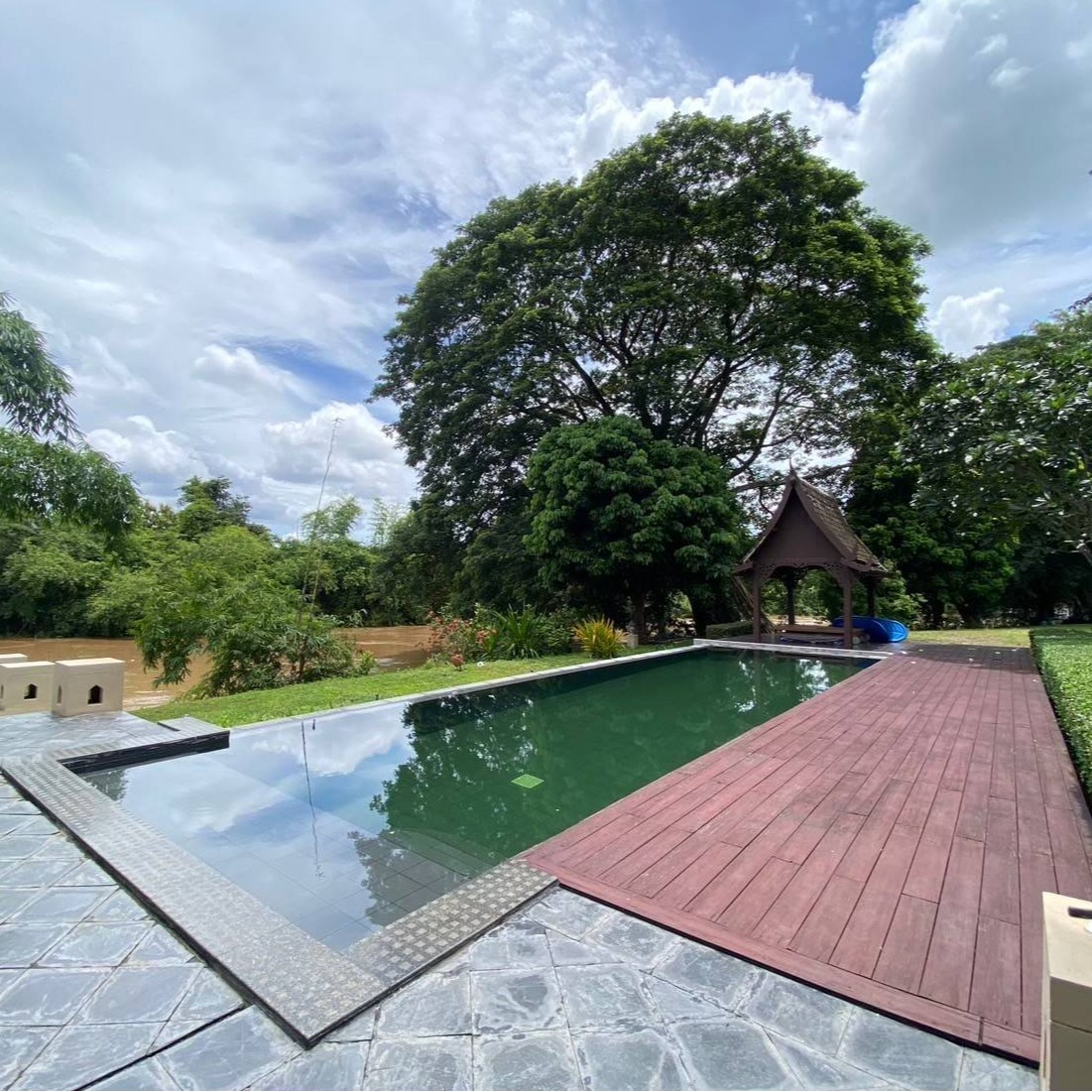 A photorealistic image of a luxury house in Chiang Mai, Thailand with a focus on the amenities.  The image should show a private swimming pool, a separate guest house, and a maid's quarters. The house should be well-lit and stylish, and the surroundings should be impeccably landscaped.  The image should evoke a feeling of comfort and high-end living.
