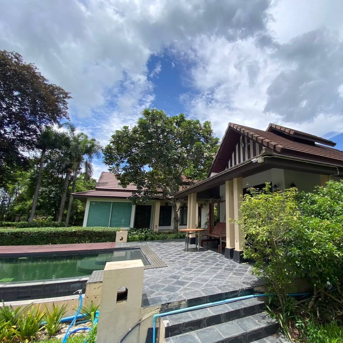 A photorealistic image showcasing the privacy and luxury of the property.  Focus on the spaciousness and modern amenities.  Show the exterior of the house with a large swimming pool, a separate guest house, and well-manicured landscaping that provides a sense of seclusion. Include details like high-end outdoor furniture and lighting.