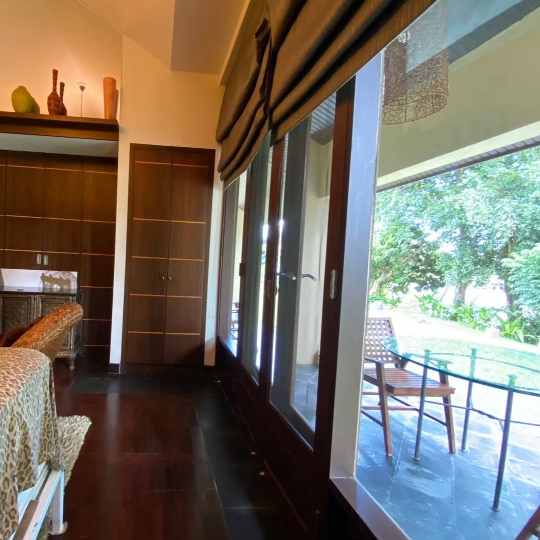 A photorealistic image of a tranquil villa nestled amidst lush greenery near a flowing river. The villa should have a traditional Thai architectural style with wooden features and a spacious outdoor area with a garden. The image should depict a peaceful atmosphere, with soft sunlight filtering through the trees and the sound of flowing water.