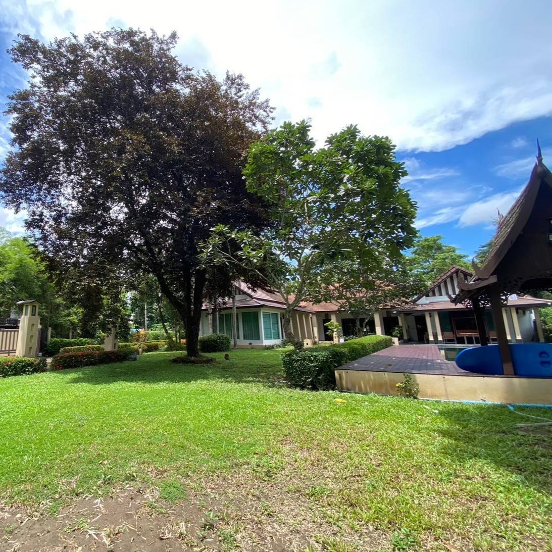 A photorealistic image showcasing the location of the luxurious villa. The image should display the villa from a distance, highlighting its proximity to the Ping River and the surrounding natural landscape. The image should also showcase the accessibility of the villa while emphasizing its serene and private setting.  The image should include a clear view of the river and surrounding lush environment.