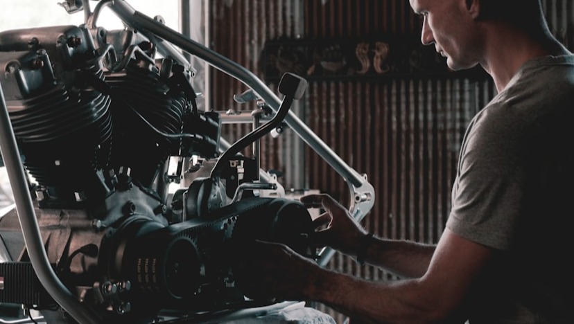 A photorealistic image of a partially completed custom motorcycle build, showcasing the frame, engine, and fuel tank. The backdrop is a clean, minimalist workshop, with diffused lighting. The motorcycle is elevated on a lift, revealing its underside. The color palette is primarily metallic, with highlights of chrome, black, and pops of vibrant color from the fuel tank. The composition is balanced and emphasizes the clean lines of the motorcycle. Texture details are crucial – the smooth finish of the fuel tank, the raw metal of the frame, the intricate details of the engine. Camera angle is slightly low, emphasizing the height and power of the build. 4K resolution, high quality.