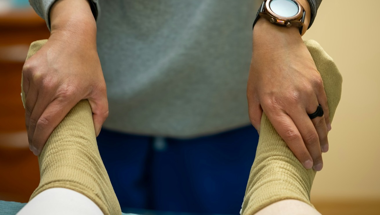 A physiotherapist guiding a patient through a specific exercise for knee rehabilitation after surgery. Focus on the controlled movement and support. The setting is a well-equipped rehab center. Lighting should be bright and focused. Color palette: Clean, medical whites and blues. Camera angle: Medium close-up, showcasing the exercise. Style: Clinical, precise. Technical Specs: 4K, High-quality.