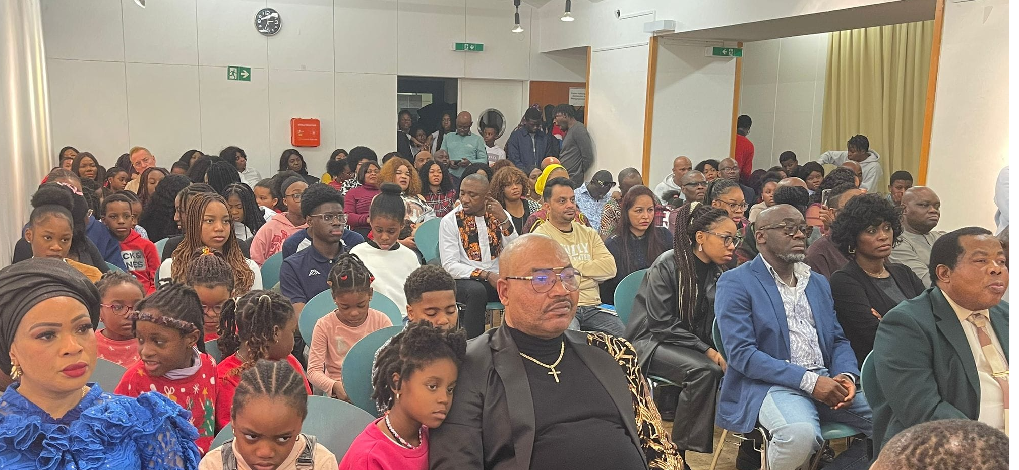 Generate a photorealistic, ultra-high definition (8K resolution) header image depicting a diverse congregation of African international people of all ages joyfully worshipping at Christ Fortress Family Church Austria.  The image should be taken during a Sunday service, bathed in the warm, golden light streaming through large stained-glass windows depicting biblical scenes. The color palette should be vibrant and uplifting, with rich, saturated colors reflecting the joy and energy of the worship. The mood is one of fervent faith, hope, and community.  The camera angle should be a slightly elevated medium shot, capturing the congregation's expressions of faith and the overall atmosphere of the service.  Textures should include the rich fabrics of clothing, the polished wood of the church pews, and the intricate detailing of the stained glass. The church interior should feature warm, earthy tones combined with the vibrant colors of the stained glass.  Visible elements might include uplifting song lyrics projected on a screen subtly in the background, and perhaps some traditional African instruments tastefully placed.  The image should be styled similar to the work of renowned photographers specializing in capturing the beauty and spirituality of religious services.  The overall feel should be hyperrealistic, aiming for a cinematic quality, similar to high-end magazine photography. The image needs to capture a sense of unity, warmth, and belonging, reflecting the welcoming spirit of the church., ultra high resolution, photorealistic, 8K, hyperdetailed, cinematic lighting