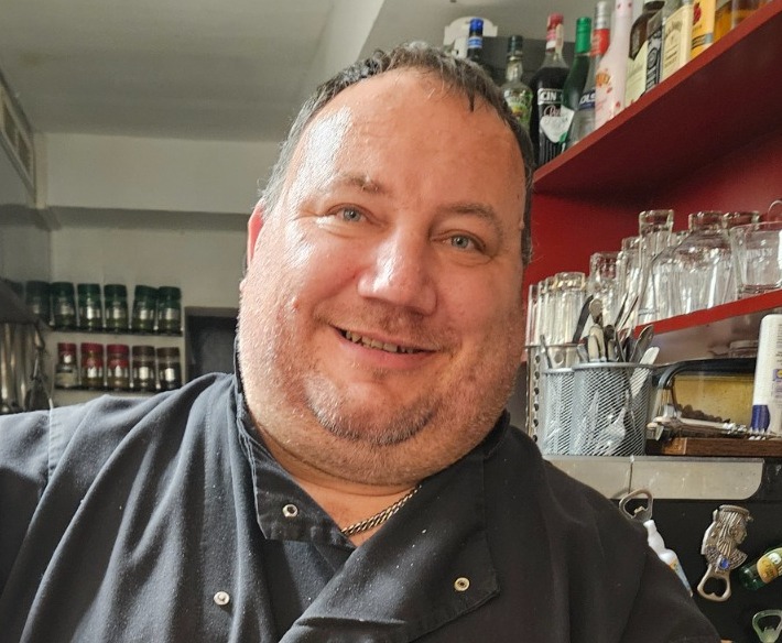 A portrait of a confident and experienced chef in their kitchen, wearing a chef's hat and apron. The background should be slightly blurred to focus on the chef's face. Convey professionalism and passion for cooking.