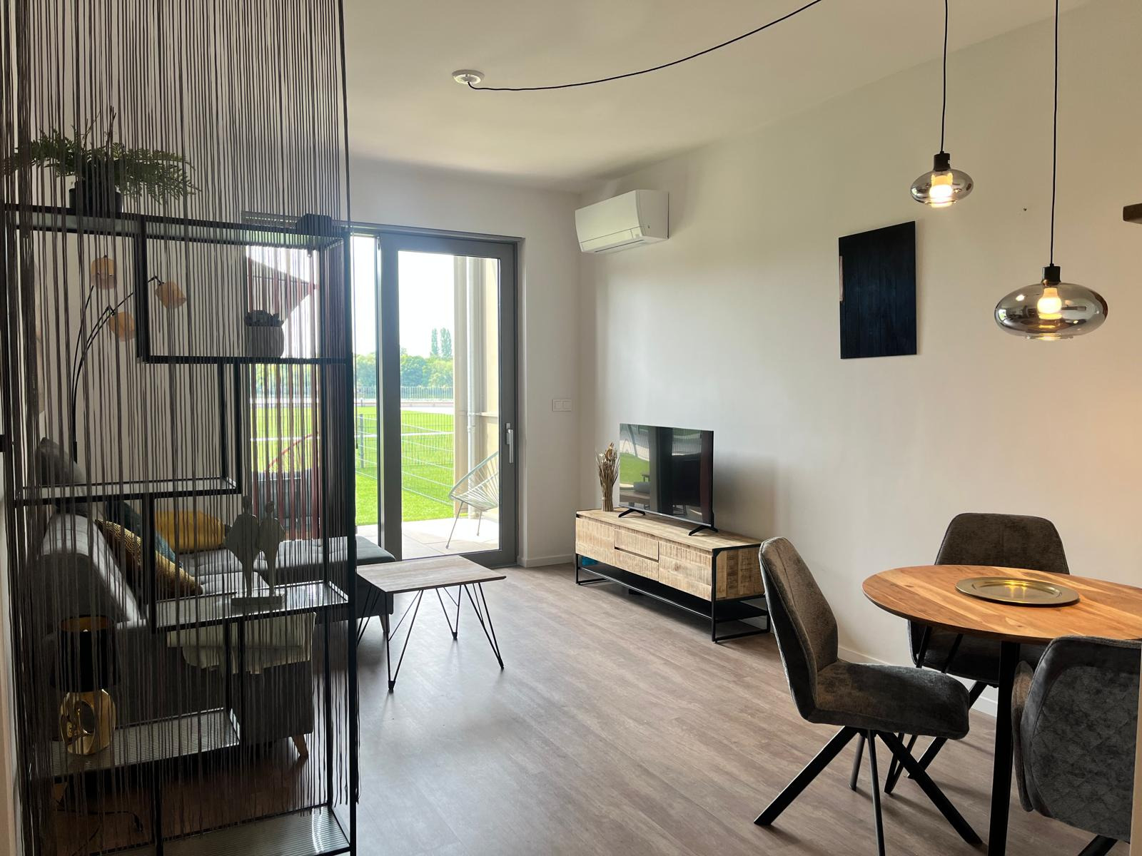 Create a photorealistic 4K image of a happy couple enjoying their stay at a holiday apartment. The image should depict a cozy living room, beautifully decorated, with large windows showcasing the sunny day. The couple should be interacting warmly, maybe sipping coffee while looking out onto the beautiful scenery. The color palette should be bright and airy, with plenty of natural light. The camera angle should be from a slightly low angle, creating a welcoming perspective. The lighting should be natural and warm, creating a cozy and inviting atmosphere. The image should capture details, such as plush cushions, warm-toned hardwood floors, and artwork on the walls, adding to the welcoming sense of home. Style should be similar to lifestyle photography showcasing comfortable home environments.