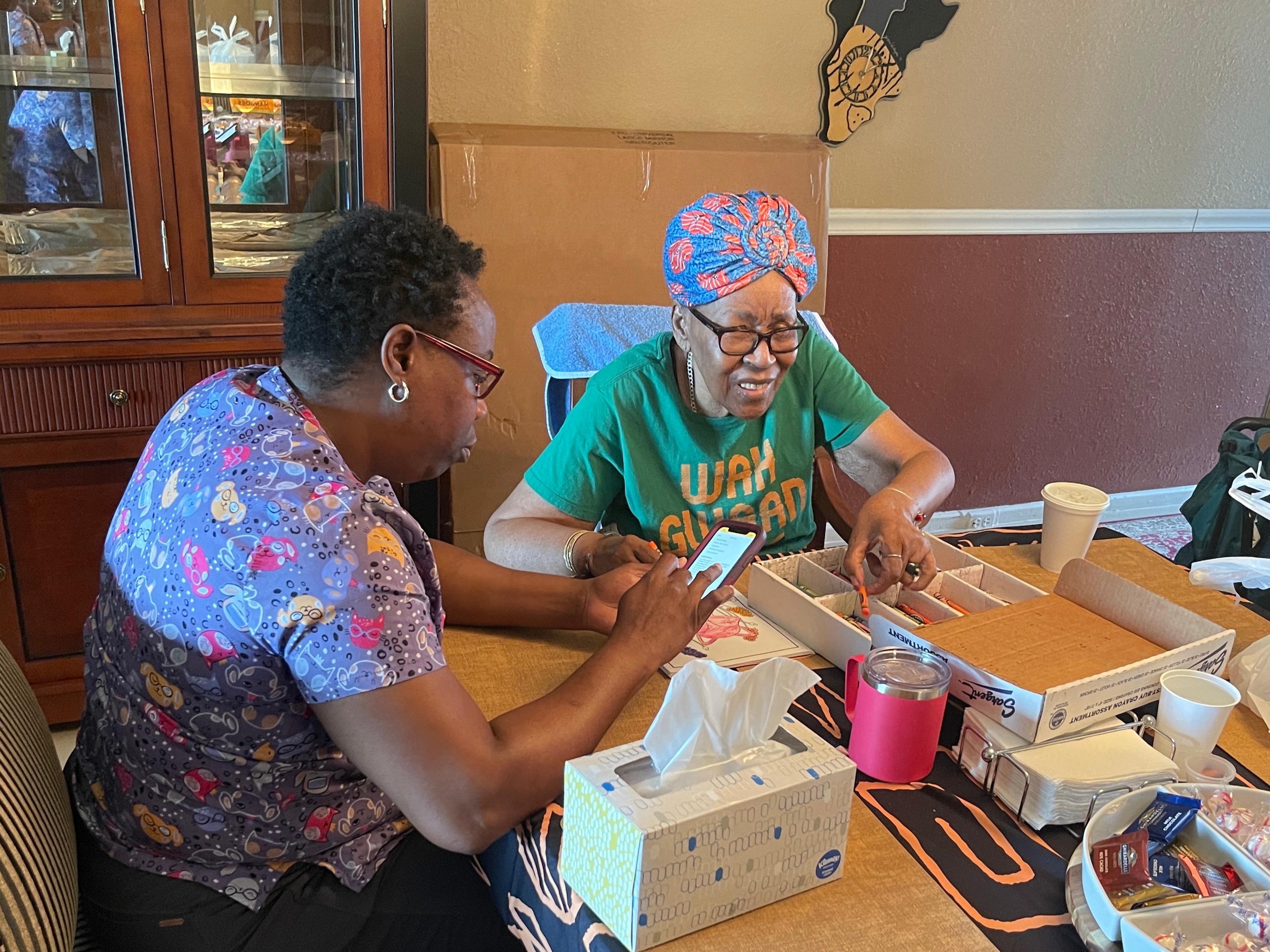 An engaging image showcases Tina Brown assisting an elderly lady in her cozy living room, helping her with activities like knitting. The soft, warm tones of the room create a peaceful environment, while family photos and homey decorations enhance feelings of nostalgia and comfort, visually communicating the idea of 'home'.