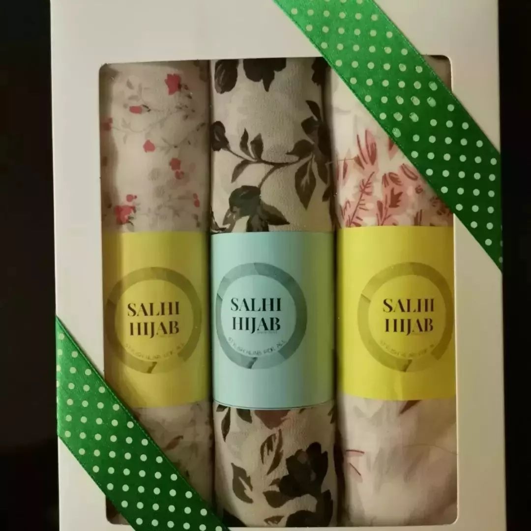 A photorealistic image of a seamstress carefully altering a hijab. The lighting is soft and focused, highlighting the precision of her work. The color palette is muted and professional. The setting is a well-equipped sewing studio. Technical specs: high resolution, shallow depth of field, focus on the seamstress's hands and the details of the fabric.