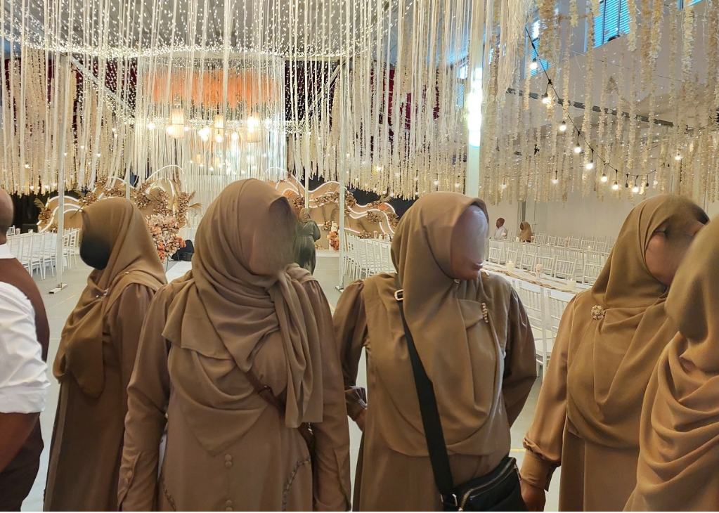 A close-up shot of a designer's hands sketching a hijab design. The background is filled with fabric swatches and design tools. The lighting is bright and focused. The color palette is vibrant and creative. Style reference: fashion design photography. Technical specs: high resolution, macro lens, focus on the details of the sketching process.