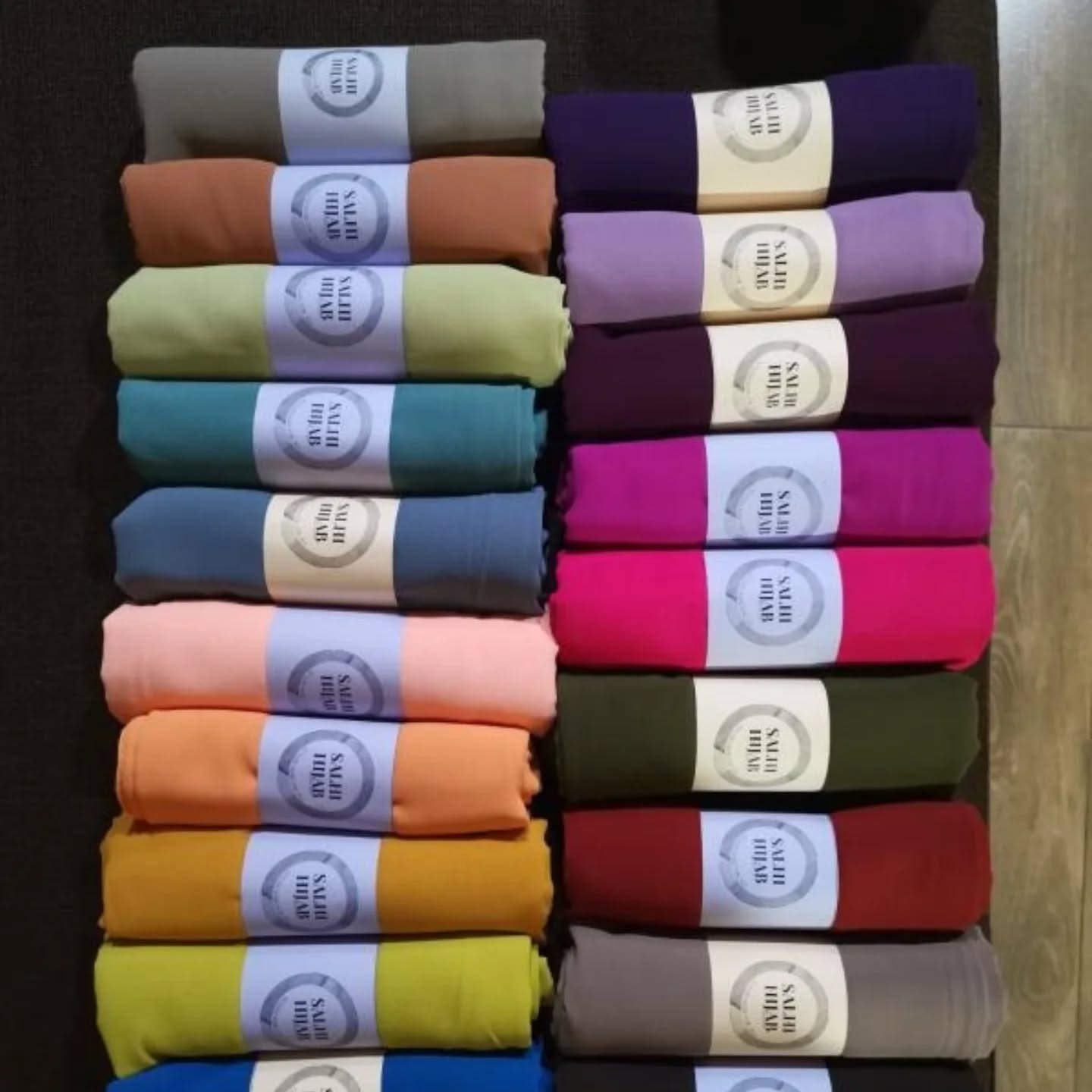 A close-up shot of a designer's hands sketching a hijab design. The background is filled with fabric swatches and design tools. The lighting is bright and focused. The color palette is vibrant and creative. Style reference: fashion design photography. Technical specs: high resolution, macro lens, focus on the details of the sketching process.