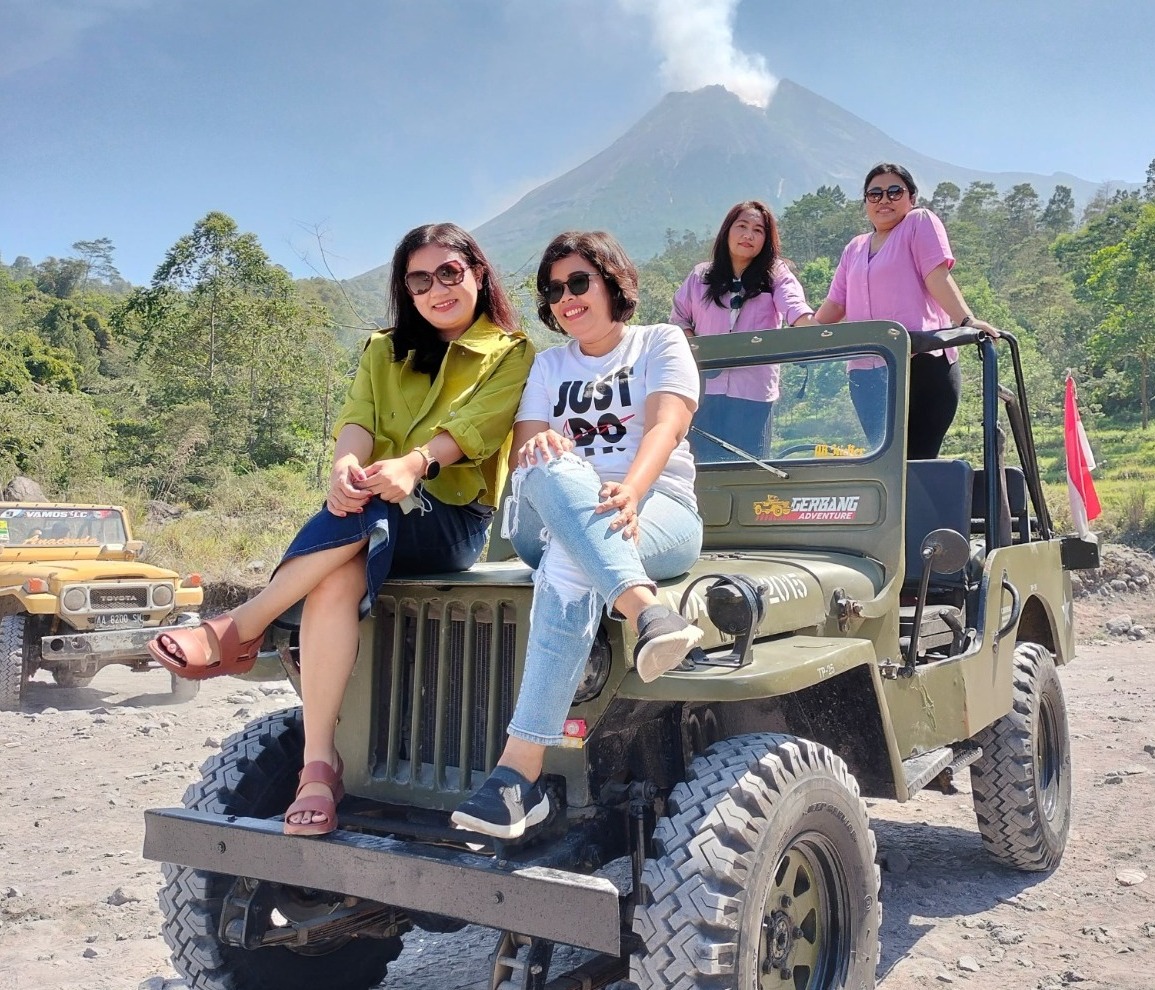 A photorealistic or stylized image representing the essence of 'Jasa Tour Jeep Merapi'. The scene features a group of excited tourists in a Jeep, smiling and interacting while traversing rugged terrains of Mount Merapi. The background showcases the majestic volcano with lush greenery surrounding it, highlighting the thrill of adventure. The lighting should be warm and inviting, capturing the joy and excitement of exploration. The angle may be slightly elevated, giving an overview of the Jeep and the landscape. Relevant props like binoculars, cameras, and maps could be included to enhance the adventurous vibe. The style should be engaging and inspirational, aiming for 4K resolution for high detail in facial expressions and surroundings.
