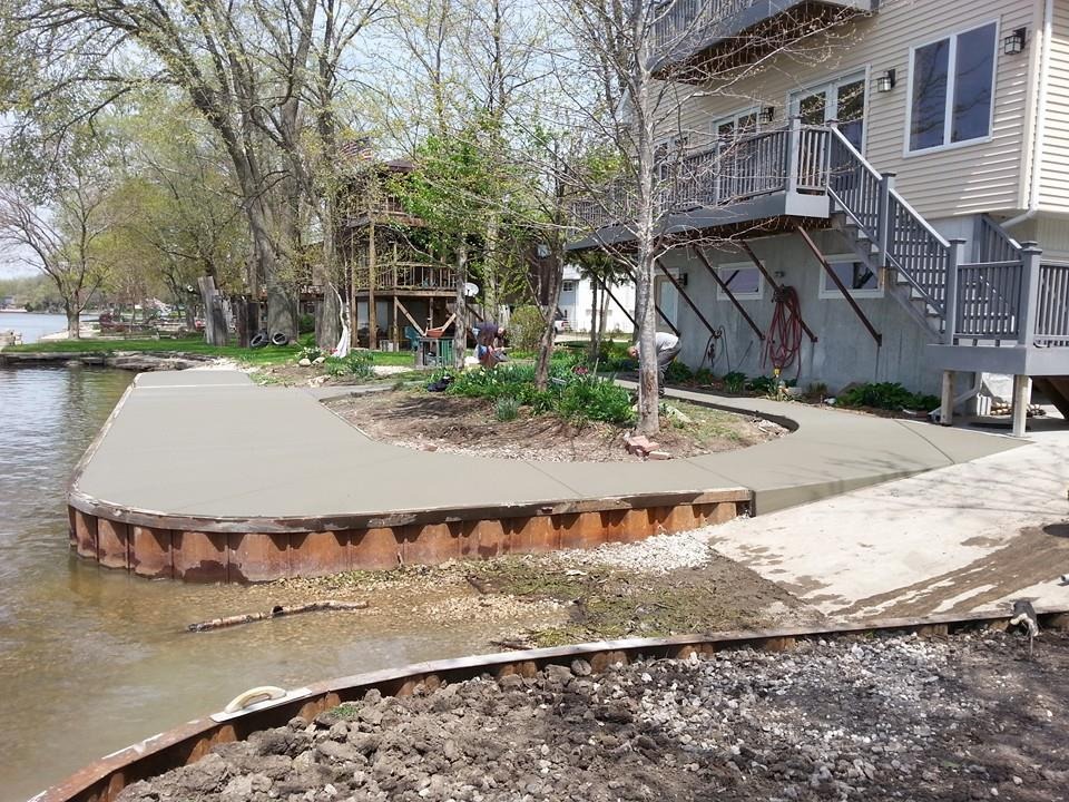 Create a 4K photorealistic image depicting a close-up of skilled hands meticulously smoothing freshly poured concrete. The concrete should be part of a residential driveway, with a blurred background showing a modern house with landscaping. The lighting should be soft and warm, highlighting the texture of the concrete and the precision of the trowel work. Include elements such as a level, knee pads, and other concrete finishing tools subtly placed. The overall color palette should be natural and earthy, emphasizing the connection between the built environment and its surroundings. Focus on conveying a sense of craftsmanship, dedication, and attention to detail, reflecting D Oxley Construction Inc's commitment to quality.