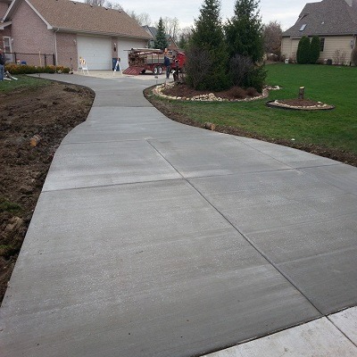  Generate a photorealistic image of a newly poured, smooth concrete driveway leading up to a modern suburban home. The sun is setting, casting long shadows and highlighting the clean lines of the driveway. Include neatly trimmed landscaping alongside the driveway. Use a warm color palette to emphasize the welcoming feel.