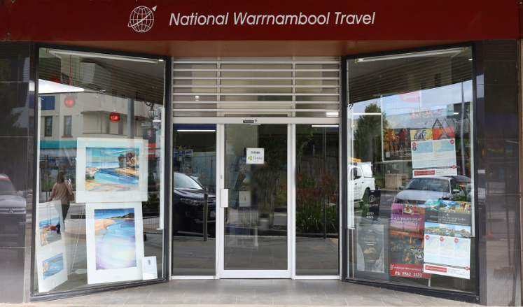 Create a welcoming, stylized image representing the heart of National Warrnambool Travel. Depict a friendly travel agent assisting a diverse group of people, planning their dream vacation. The background should subtly showcase iconic Warrnambool landmarks, such as the whale watching platform and the Flagstaff Hill Maritime Village. Use a warm, inviting color palette with soft lighting to create a sense of trust and excitement. The composition should be balanced and visually appealing, with a focus on the interaction between the agent and the travelers. Style: Modern illustration with realistic touches. Technical specs: 4K resolution, high detail, vibrant colors.