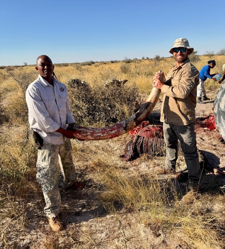 A portrait of an experienced African guide, weathered and wise, with a kind smile. He is wearing traditional safari attire and holding a pair of binoculars. Focus on his knowledge, experience, and connection to the land. 4K resolution, high detail.