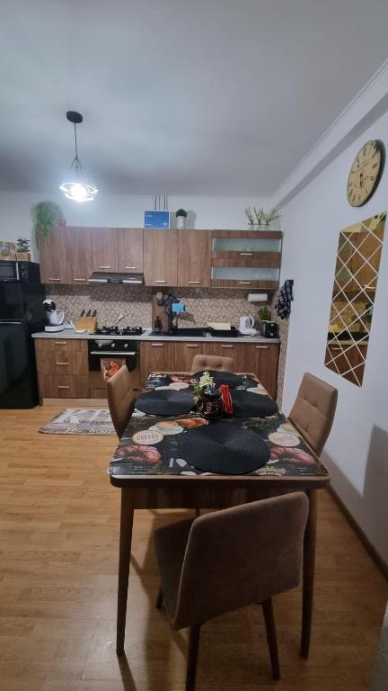 Showcase the kitchen in "Casa cu 2 Dormitoare La Simo". The scene focuses on modern appliances seamlessly integrated into a rustic design. A large window overlooks the garden. Sunlight illuminates the space. The color palette is a blend of natural wood tones and clean white surfaces. Stainless steel accents add a touch of modernity. Capture the textures of the wood, the tiles, and the metal. The lighting should be bright and inviting. Aim for a photorealistic, high-quality image.