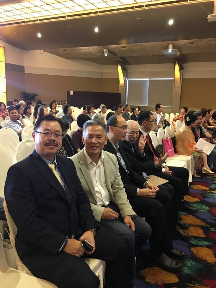A photorealistic image of a networking event at the Feng Shui conference. Attendees are mingling and chatting with smiles. The background is a modern, well-lit event space with East Chen Consultancy branding subtly displayed. The lighting is warm and inviting, fostering a sense of community. The camera angle is a medium shot, capturing the energy and connections being made. Use a 4K resolution to capture the details of the interactions and the environment.