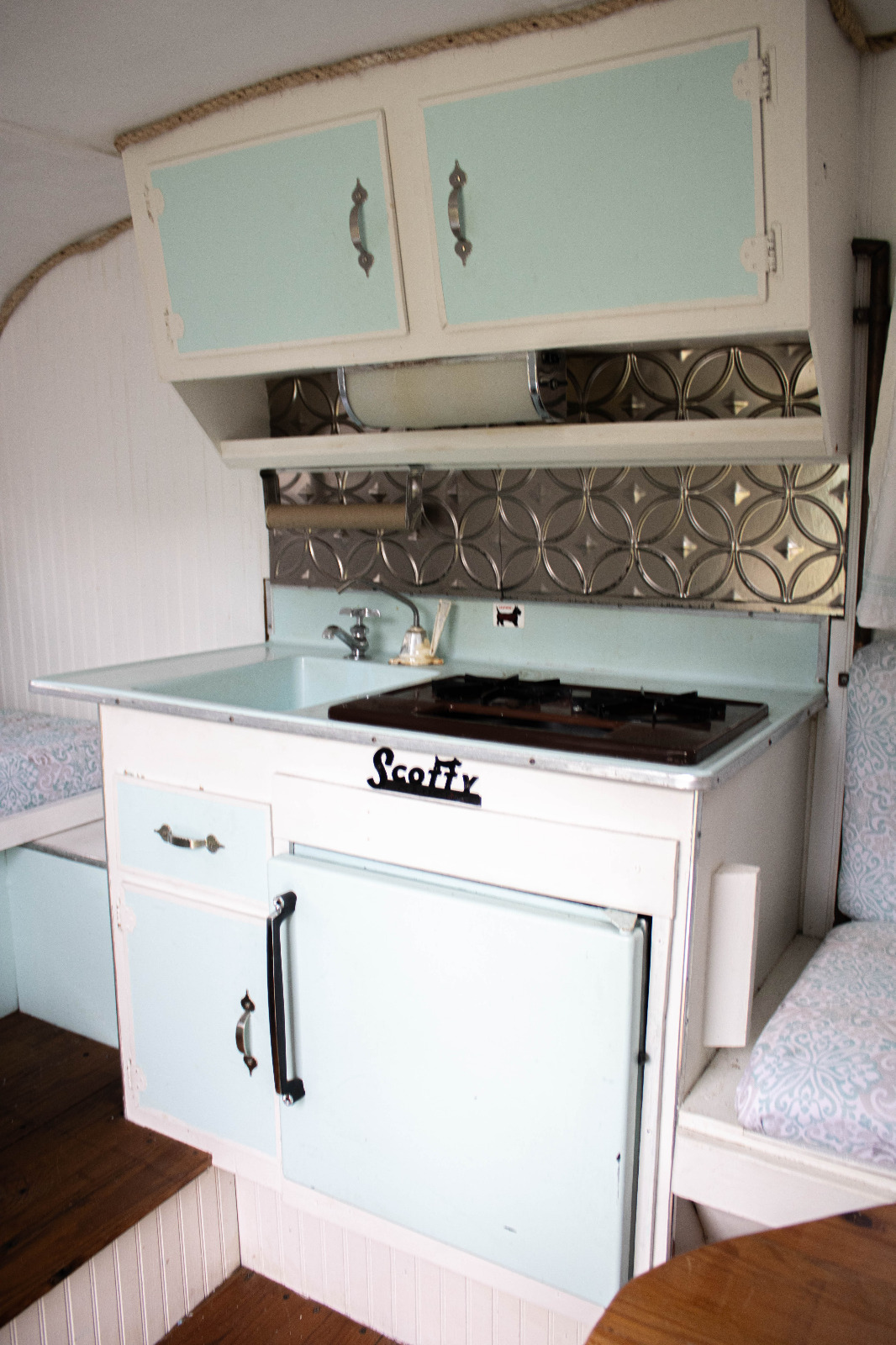 A wide shot of the Blue Sky Day photo booth trailer parked at a lively outdoor event. Guests are happily lined up, waiting their turn to enter. An assistant is smiling and interacting with the guests, ensuring a smooth and organized experience. The background is filled with festive decorations and excited attendees. The lighting should be natural and bright, capturing the energetic atmosphere of the event. Style reference: A candid, documentary-style photograph showcasing the seamless integration of the photo booth trailer into a real-world event.