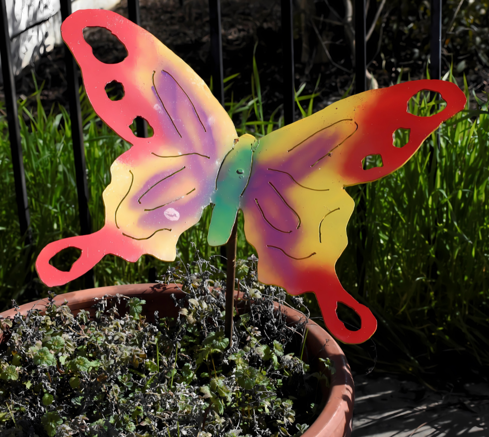 A vibrant photograph of several Metal By Mark yard stakes depicting whimsical animals (birds, butterflies, etc.) planted in a colorful flower garden. The stakes are made of brightly painted metal. The image should convey a sense of joy and whimsy.