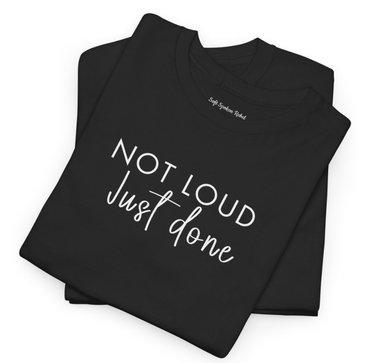 Create a stylized image featuring a Soft Spoken Rebel t-shirt with a bold design laid out on a soft, fluffy blanket. The lighting is soft and diffused, creating a warm and inviting atmosphere. The color palette is pastel and muted, with pops of vibrant color in the design of the t-shirt. The overall feel is cozy and comforting, conveying the idea of gentle rebellion. Technical specs: 4K resolution, high quality, soft focus.