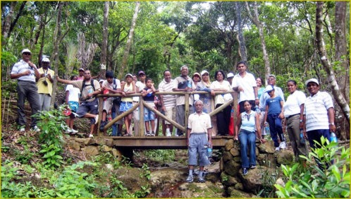 A photorealistic shot of MRASWA members helping each other over a rocky part of a trail. Smiling faces and encouraging gestures emphasize camaraderie. Bright daylight, clear focus. 4k resolution.