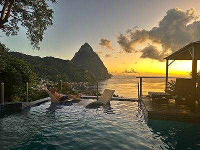 Create an image of a luxurious resort in Saint Lucia, showcasing its stunning views and amenities. The lighting should be warm and inviting. The color palette should emphasize the blues of the ocean, the greens of the gardens, and the whites of the buildings. Capture the essence of a relaxing vacation in Saint Lucia in 4k resolution.