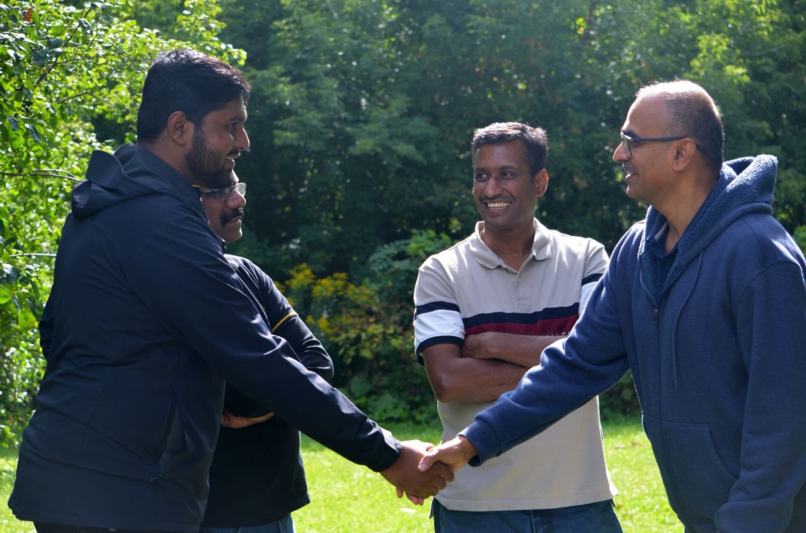 Create a photorealistic image of people shaking hands at a Kammavar gathering, symbolizing connection and networking. Focus on genuine smiles and positive body language. The background could be a modern convention hall or a friendly outdoor event. The lighting should be bright and cheerful. 4K resolution, high quality.