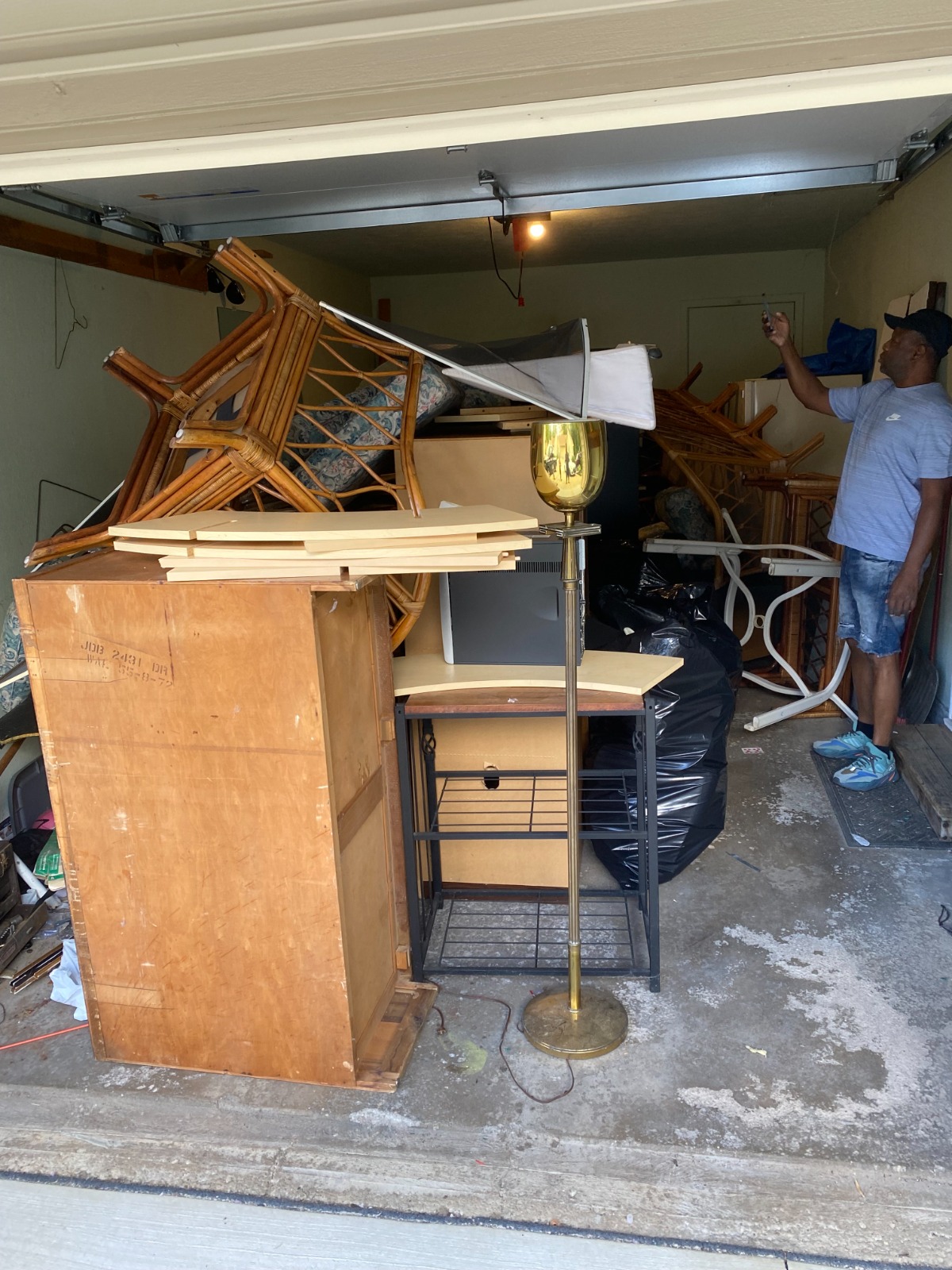 An organized garage or yard with several labeled bins for recycling, trash, and donations. A family is sorting through boxes, putting items into each bin. There are cluttered boxes in the background, highlighting the cleaning process.