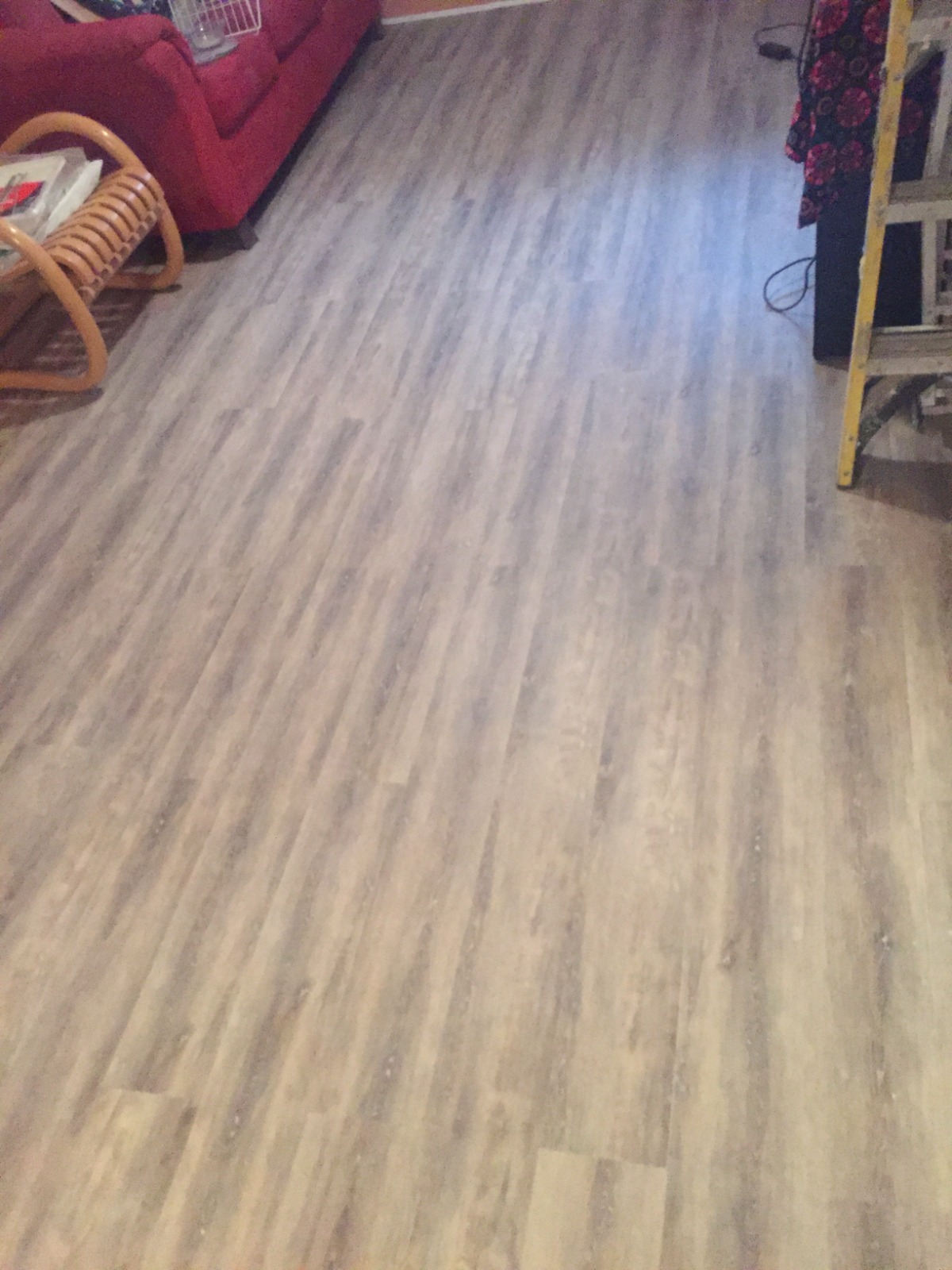 A close-up view of a modern kitchen floor with shiny vinyl plank flooring being cleaned. A person is using a mop with a bucket filled with soapy water, demonstrating effortless upkeep, with sunlight streaming through a nearby window reflecting off the clean surface.