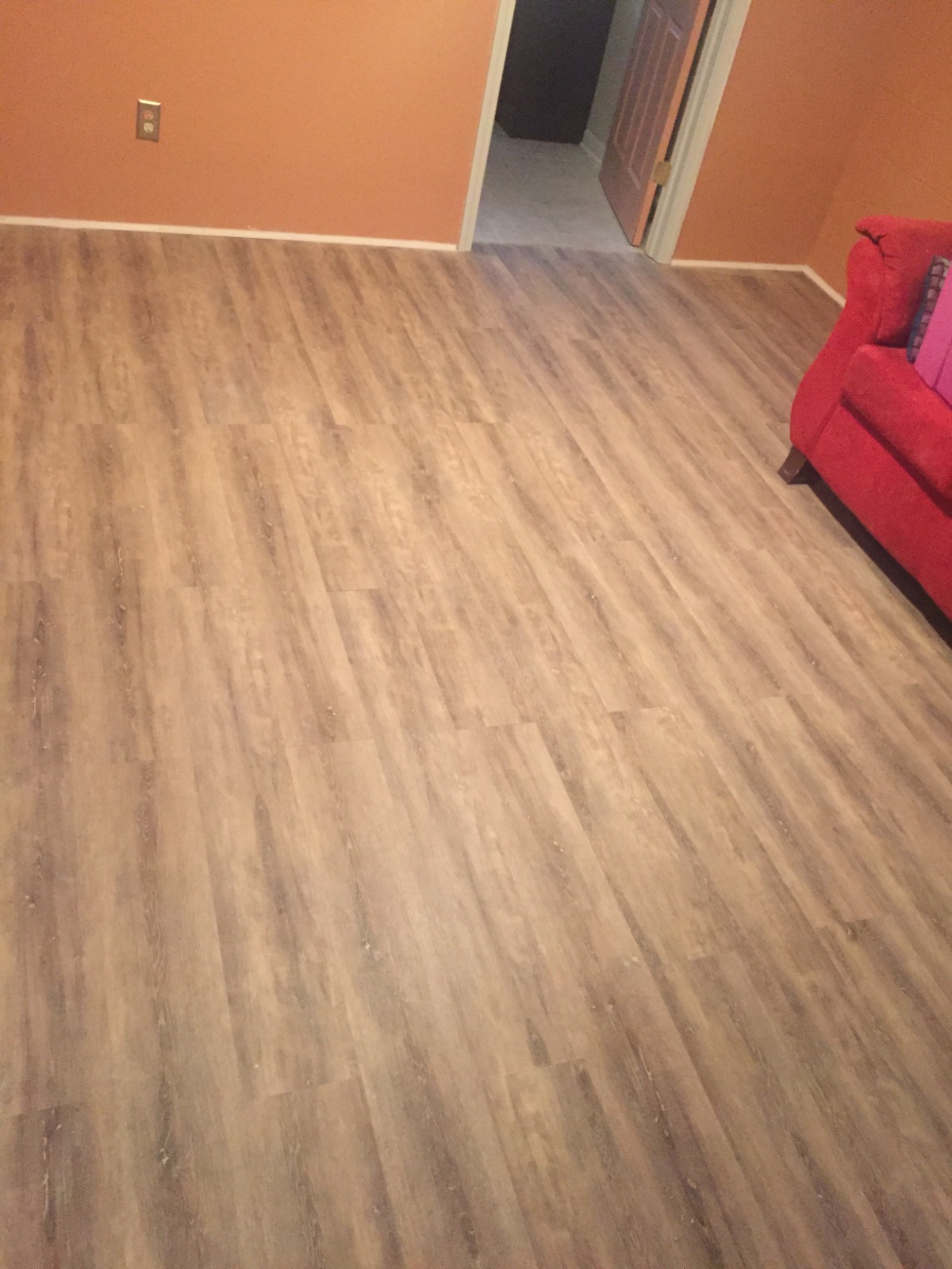 A photorealistic interior scene showcasing a stylish living room with natural light, featuring durable vinyl plank flooring that resembles warm oak wood. The room is tastefully decorated with modern furniture and green plants, highlighting the elegance and practicality of vinyl flooring.