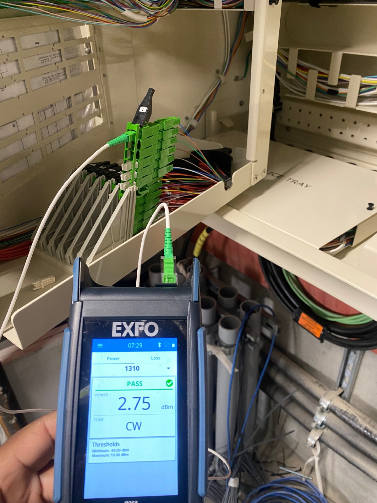 A technician using an OTDR (Optical Time-Domain Reflectometer) to test a spliced fiber optic cable. The OTDR screen should display a clear graph of the signal. Lighting should be soft and focused on the screen. Style: Practical, professional, and reliable.