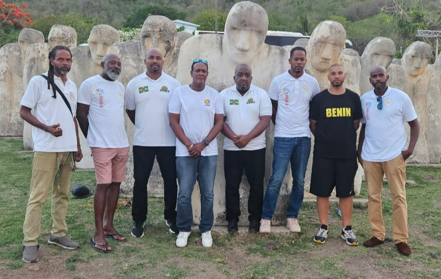 A symbolic image featuring a diverse group of people holding hands in a circle, surrounding a large basketball. The backdrop includes serene landscapes of Martinique and Guadeloupe, along with elements representing unity, peace, and shared aspirations.